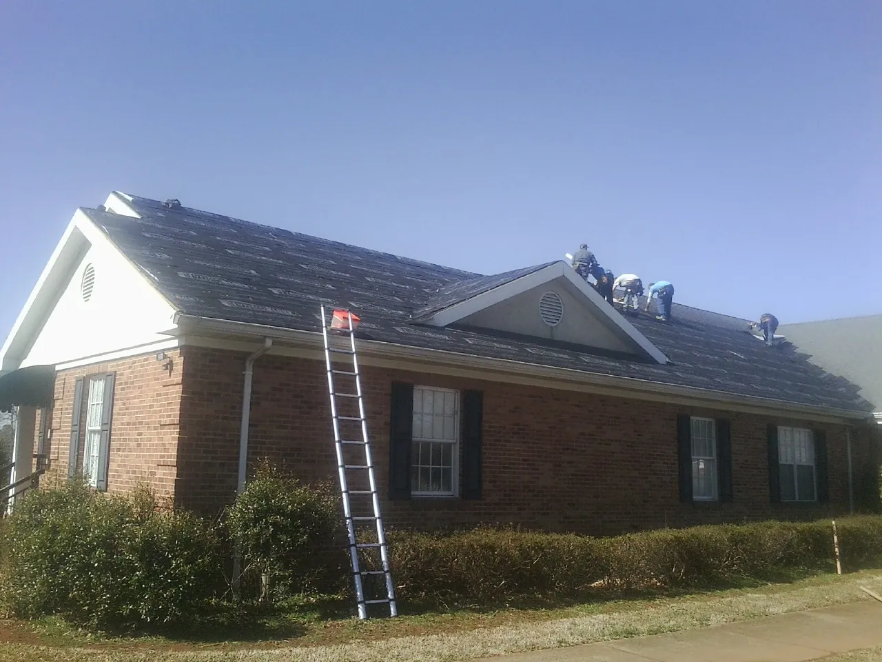 Crew tearing shingles off a brick ranch roof with a ladder set — Emergency Roof Repair work by our crew in Russell Springs