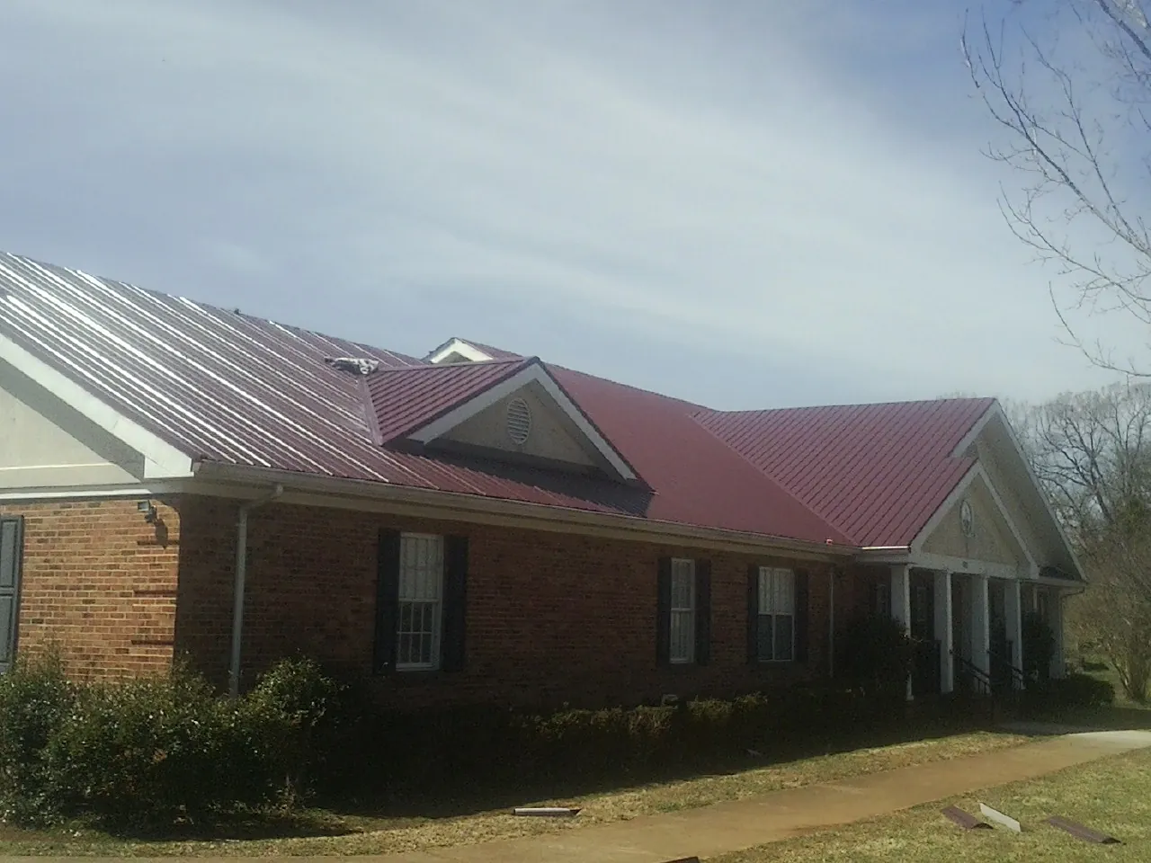 Red metal roof with gabled entries on a long brick building, from a Hail Damage Roof Repair job in Russell Springs