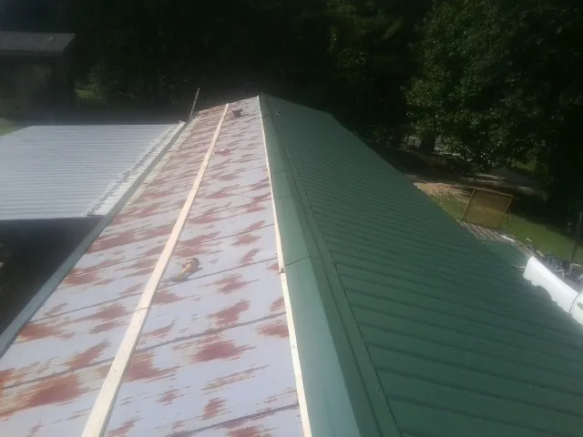Old rusted panels beside newly installed green metal roofing — Wind Damage Roof Repair by Roofing Brothers in Russell Springs