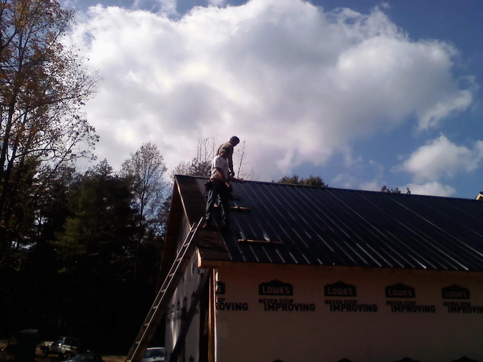 Roofer fastening dark metal panels high against a cloudy sky, from a Roof Inspection job in Russell Springs