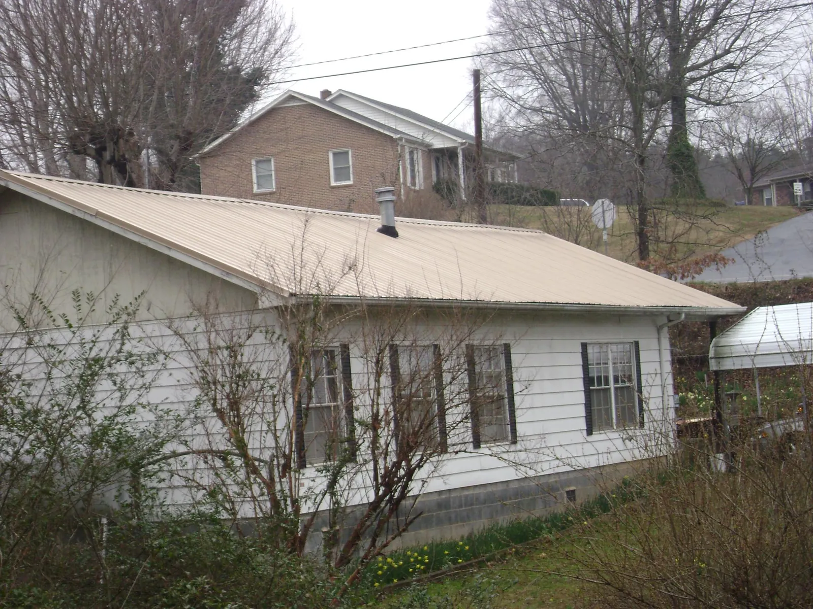 Tan metal roof on a white sided house set into a hillside — Commercial Roofing by Roofing Brothers in Russell Springs